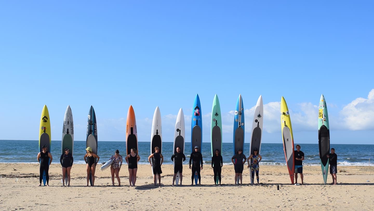 Paddleboard competitors lined up on the beach with boards